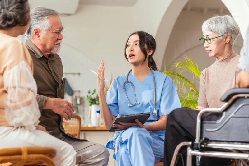 happiness-cheerful-elderly-woman-men-talking-with-female-caregiver-nurse-doctor-having-health-checking-consult-living-areacaretakers-with-senior-couple-sitting-living-room-nursing-home