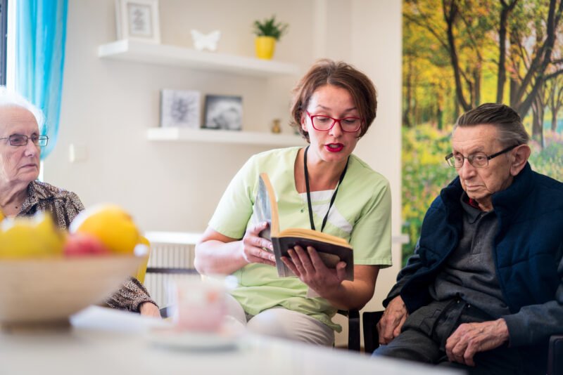 Nurse reading book to elderly group of people