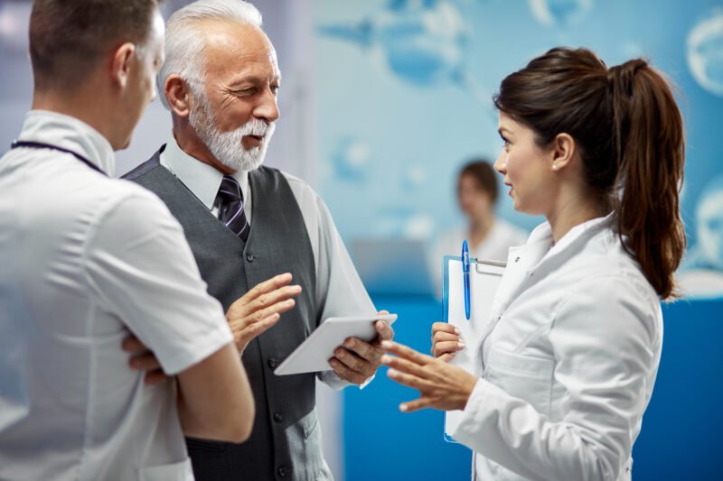 Happy senior businessman talking to doctors in hallway at the ho Happy senior businessman talking to doctors in hallway at the ho