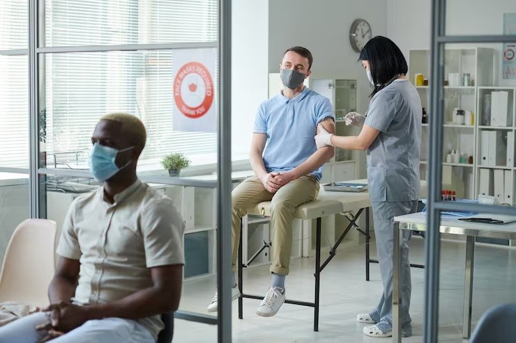 imgi 7 brunette nurse uniform protective mask making injection young man sitting medical office while african guy waiting his turn 2746